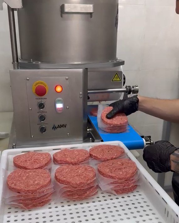 Máquina da Fernandez moldando hambúrgueres, com bandeja de hambúrgueres padronizados em primeiro plano